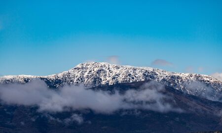 Mountains full of trees and  clouds cover the tops of snowy mountains