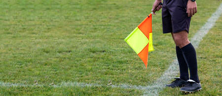 Football soccer arbiter assistant with flag at hands. Blurred green field background, close up.の写真素材