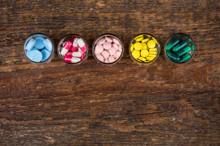 Various pills and capsules in glass containers on wooden tableの写真素材