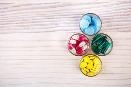 Various pills and capsules in glass containers on light wood tableの写真素材