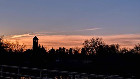 colorful distinct sunrise photo with sillouetted foliage and clock towerの写真素材