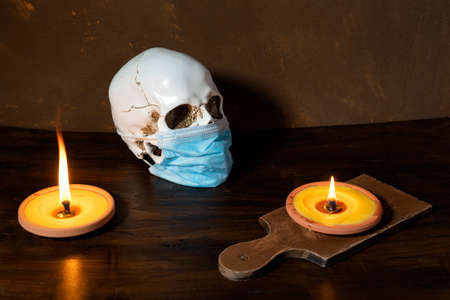 human skull in medical mask wooden background, with burning candles