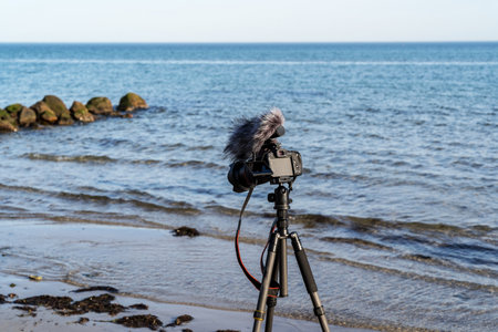 A camera is on a tripod on a beach. The camera is recording the ocean and the beach