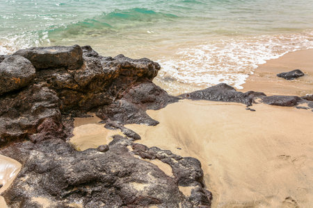 A rocky beach with a large rock in the foreground. The water is calm and the sky is clear