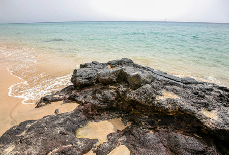 A rocky beach with a large rock in the foreground. The water is calm and the sky is clear