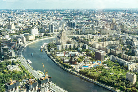 A Moscow city with a Moscow river running through it. The river is surrounded by buildings and trees. There are boats on the river and a crane in the backgroundの写真素材
