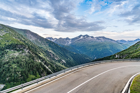 A mountain range in Swiss Alps with a road in front of it. The road is empty and has a white line down the middleの写真素材