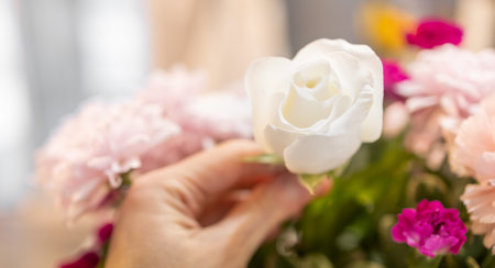 Hand holding a blooming white rose with blurred colorful floral background, mixed flowers bouquet for decoration at a romantic wedding celebration. Happy moment, the sweet love concept. Valentines dayの写真素材