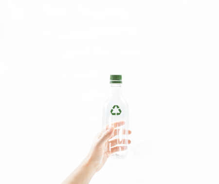 Personâs hand hold an empty transparent water bottle with green recycle symbol on white background. Concept of care, responsible, recycling and save the environment and world from global warming.の写真素材