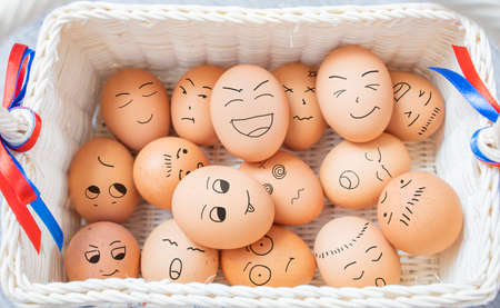 Eggs with different mood expressions by draw humor cartoon face on eggshells heap in weave basket, a symbol of Easter as a fun traditional holiday in April. Creative idea concept of group gathering.の写真素材