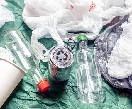 Bottles, beverage takeaway paper cup, plastic glass, aluminum container and plastic bags on green background. Recycle and reusable waste management. Concept of environmental responsibility and care.の写真素材