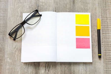 Top view, white blank notebook with colorful  sticky notes, yellow pen and eyeglass flat lay on...