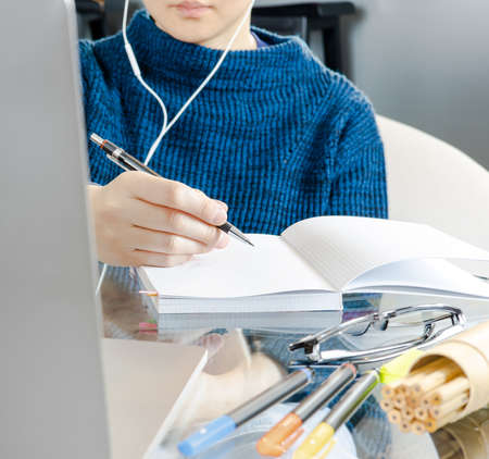 Young student with earphones taking lecture on blank page while learning online via laptop. Freelance plan project during virtual meeting at coffee shop. Concept of remote study and work from home.の写真素材