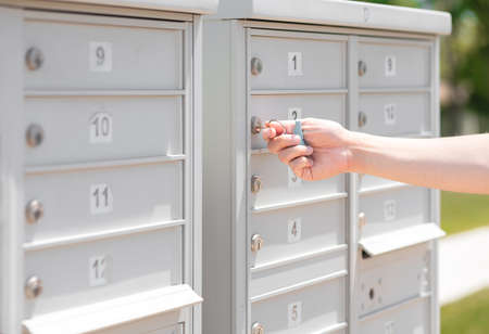 Personâs hand holding key unlock-lock mailbox by house number, selective focus. Receiver get mail and small parcel from row of outdoor metal storage, depth of field. Man close residential letterbox.の写真素材