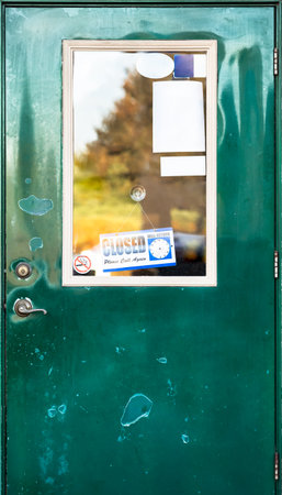 Closed sign hanging and some white paper notice stick on a glass window of weathered green front door. Antique shop temporary shut during crisis. Break time hour for vintage retail business. Shutdown.の写真素材