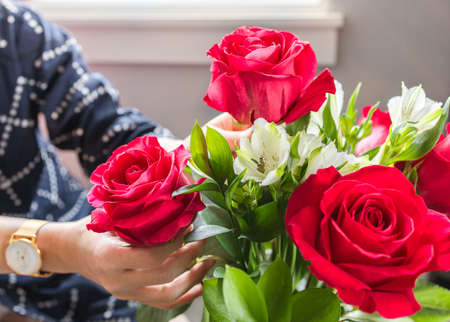 Woman florist hands making mix fresh flowers with green leaves for special anniversary. Closeup bunch of beautiful blossom red roses, depth of field. Arranging for wedding bouquet. Specialist concept.の写真素材