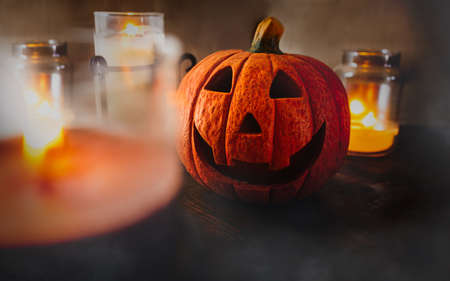 Halloween pumpkin smile among candle lights with soften smoke on wooden floor and dark brown background, depth of field. Spooky and scary traditional festival in October. Symbol of fun trick and treatの写真素材