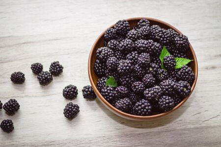 Ripe blackberries with leaves in a clay bowl on a light wooden background. Flat lay, top view. Photo...