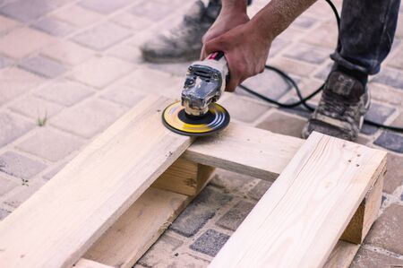 Workers hands at carpenter workspace refining the surface of wood board using sand paper grinder.の写真素材