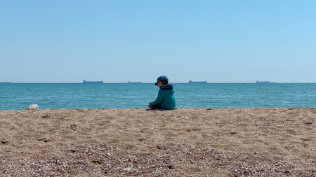 boy sitting on the beach and watching the ship in the sea.の写真素材