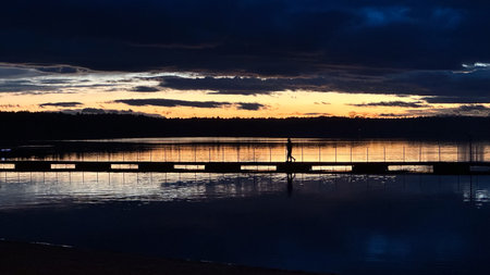Sunset over a lake with a silhouette of a man on a pierの写真素材