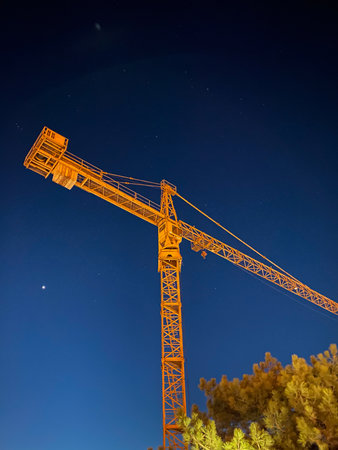 Construction crane at night with starry sky and pine trees in foregroundの写真素材