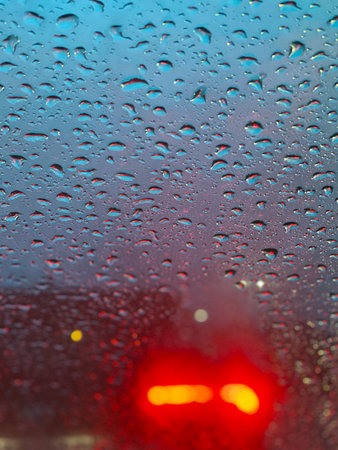 rain drops on the glass with a red car light in the backgroundの写真素材