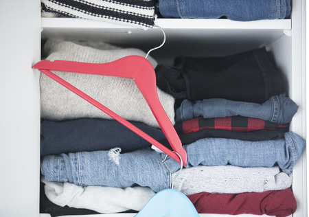 photo of stack of different colorful clothes and hangers in modern wardrobe close upの写真素材