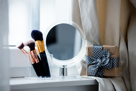 professional makeup brushes in glassy box, gift and cute mirror on the wonderful white windowsillの写真素材