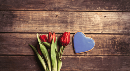 heart shaped cookie and bunch of tulips lying on the wonderful brown wooden backgroundの写真素材