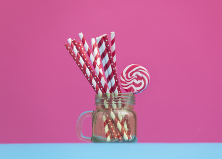 a glass jar with cocktail sticks and sweet lollipop on the wonderful pink backgroundの写真素材