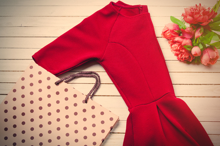 red dress, shopping bag and bunch of roses on the white wooden backgroundの写真素材