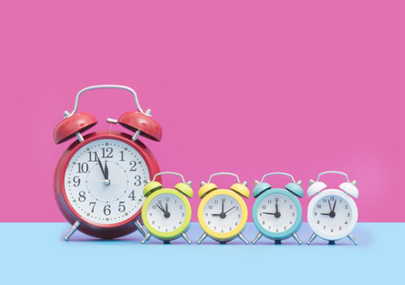 chain of cute colorful alarm clocks in front of wonderful pink backgroundの写真素材