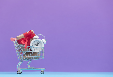 cute small gifts and alarm clock in the cool shopping cart on the wonderful purple backgroundの写真素材