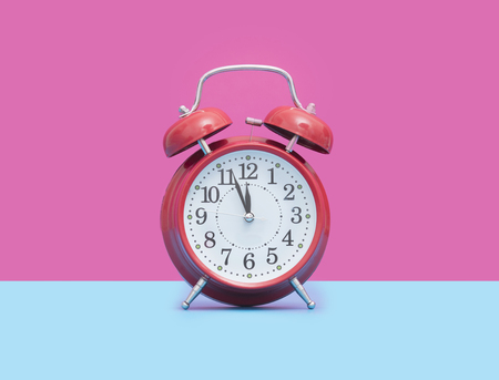 photo of cute red metal alarm clock in front of wonderful pink backgroundの写真素材