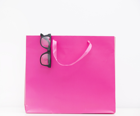 cool black glasses on the pink shopping bag on the wonderful white backgroundの写真素材