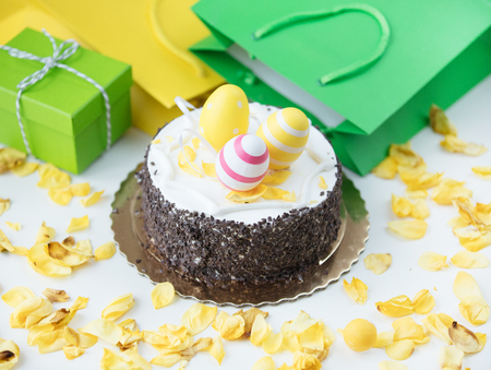 easter eggs on chocolate cake near shopping bags, gift and dried yellow rose petals