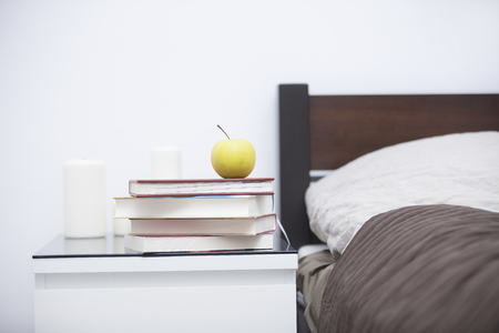 pile of books, notebook, apple and set of candles on the table near bed in the cozy bedroomの写真素材