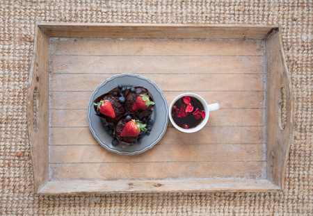 photo of delicious tasty muffins with blueberries and fresh strawberries on the top and cup of tea with petals on the board on the wonderful brown carpet backgroundの写真素材