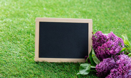 photo of blackboard and bouquet of lilac on the wonderful green grass backgroundの写真素材