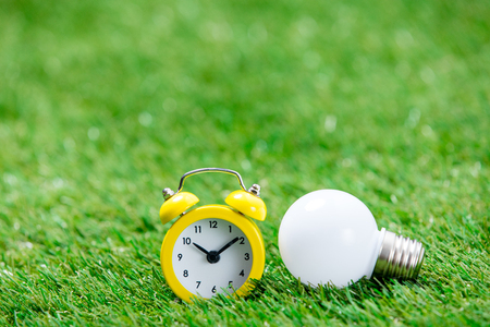 photo of alarm clock and bulb on the wonderful green grass backgroundの写真素材