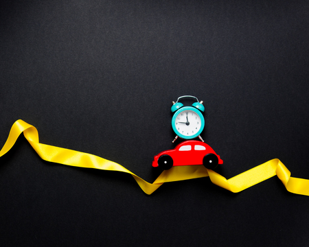 Little car with alarm clock and ribbon on black backgroundの写真素材