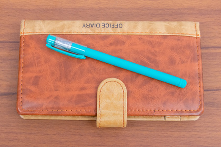 Brown business offiice diary with ball pen and glass on a light wooden background