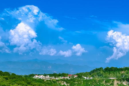 Scenic view of hills with blue  cloudy white sky, mountain covered with mist and housesの写真素材