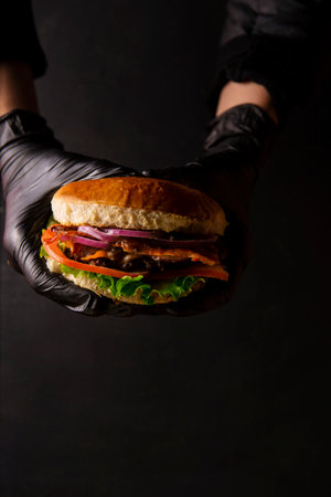 Hands in black gloves holding hamburger on a black background.の写真素材