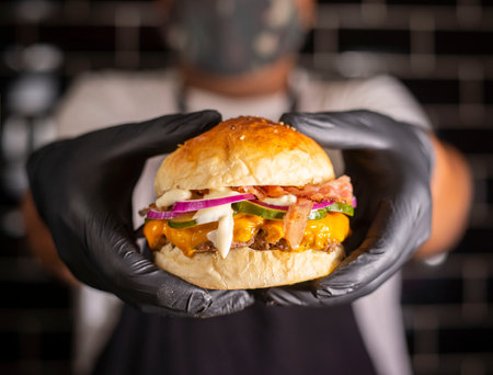 Chef in black gloves holding a cheeseburger with beef and vegetablesの写真素材