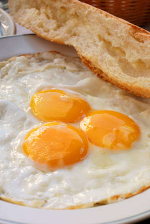 close-up of isolated three fried eggs in white plate with french fresh bread