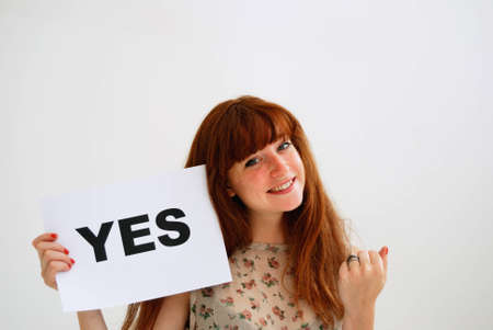 Portrait of young woman holding Yes sign against white background の写真素材