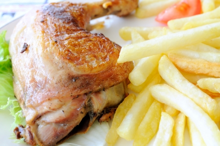 delicious isolated roasted chicken leg with white french fries in white plateの写真素材