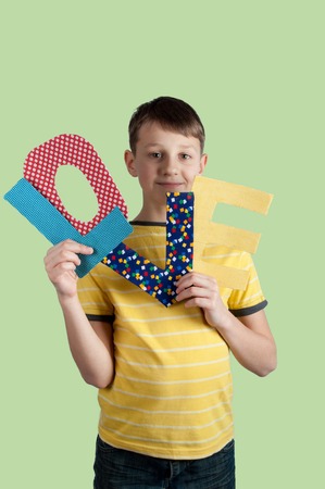 Cute young boy holding paper letters love in his hands on green background.の写真素材